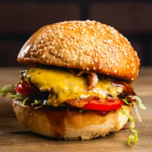 Szezámmagos kézműves hamburger, tökéletesre pirított baconnel, vörös cheddar sajttal, friss paradicsomkarikával és salátával, lilahagymával.