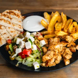 Csirke gyros tál, sült pitával és salátával és friss csónakburgonyával tálalva.